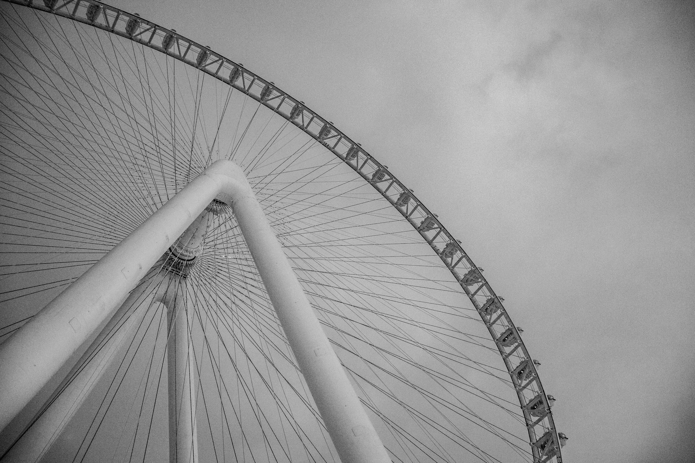 Black-and-white view looking up at Ain Dubai's spokes and cabins against a cloudy sky