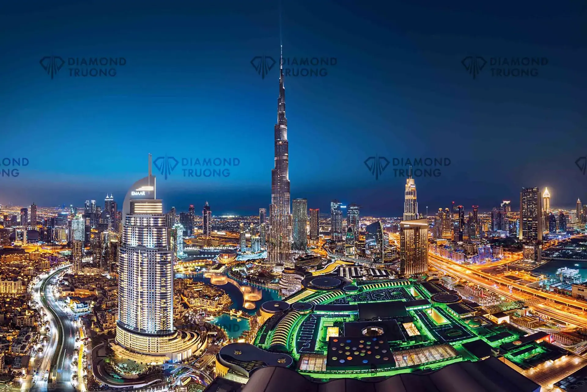 Downtown Dubai at night from above: a hotel tower and the Burj Khalifa behind Dubai Mall's lit green roof