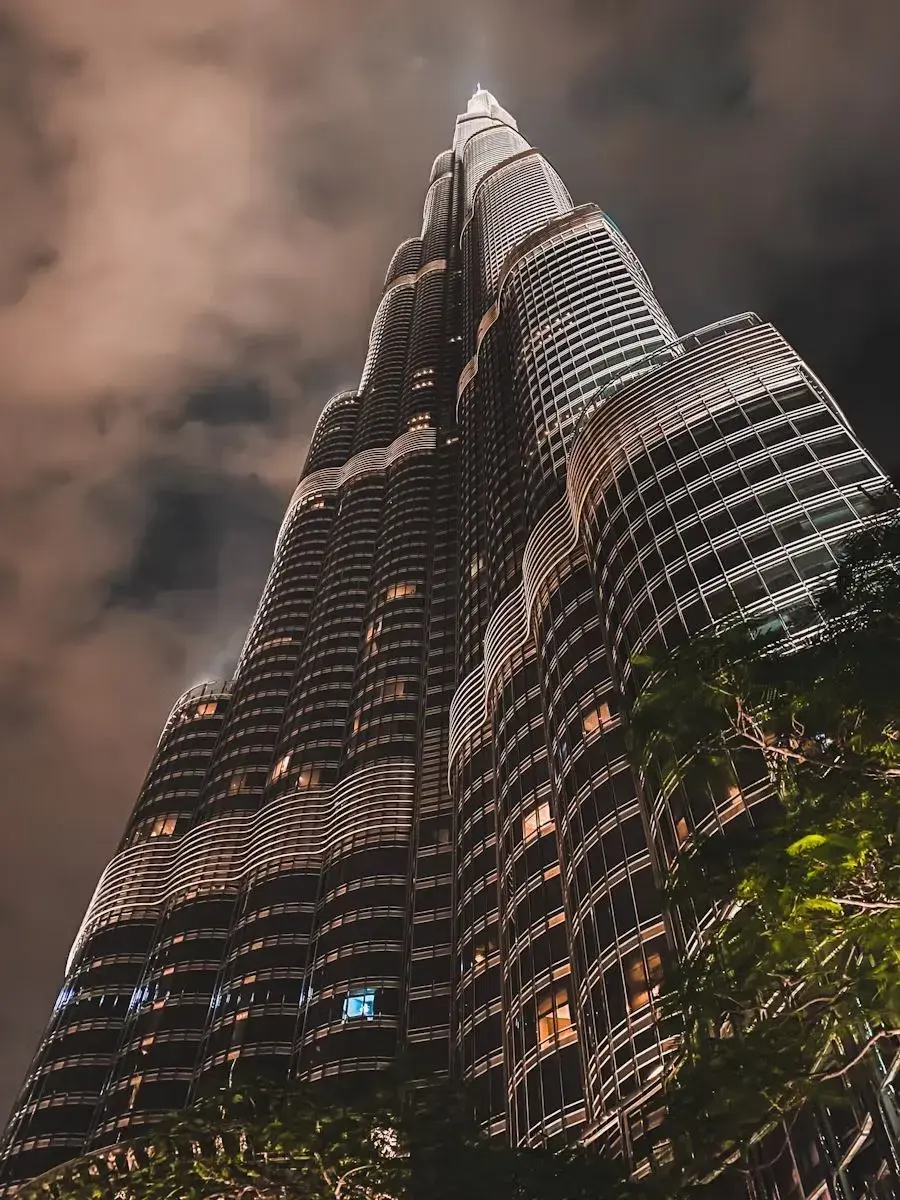 Night view looking up at the illuminated Burj Khalifa skyscraper with cloudy sky in the background.