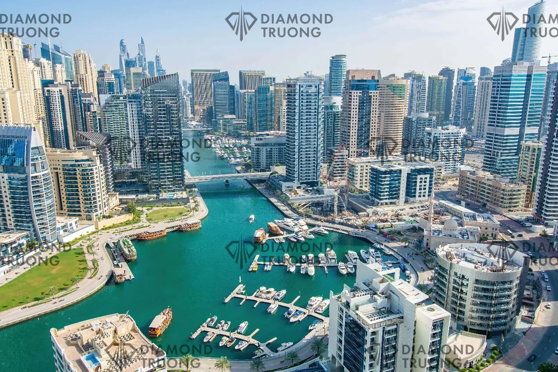 Dubai Marina from above by day: the canal with moored boats and dhows, a park on one bank and towers on both