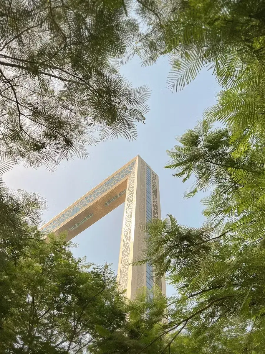 View of the Dubai Frame monument framed by green tree branches against a clear blue sky.