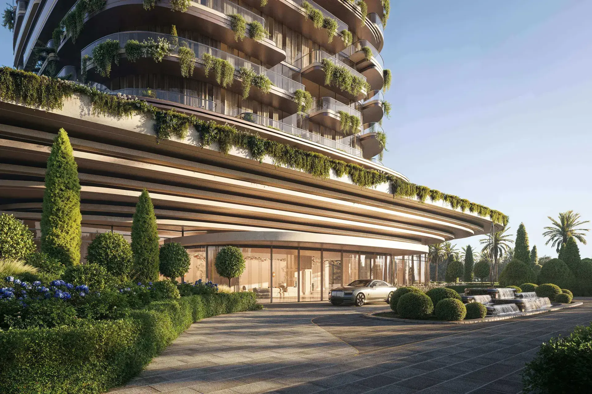 Render of the entrance: a curved canopy over a glazed lobby, a car at the drop-off, clipped hedges, cypresses and a fountain