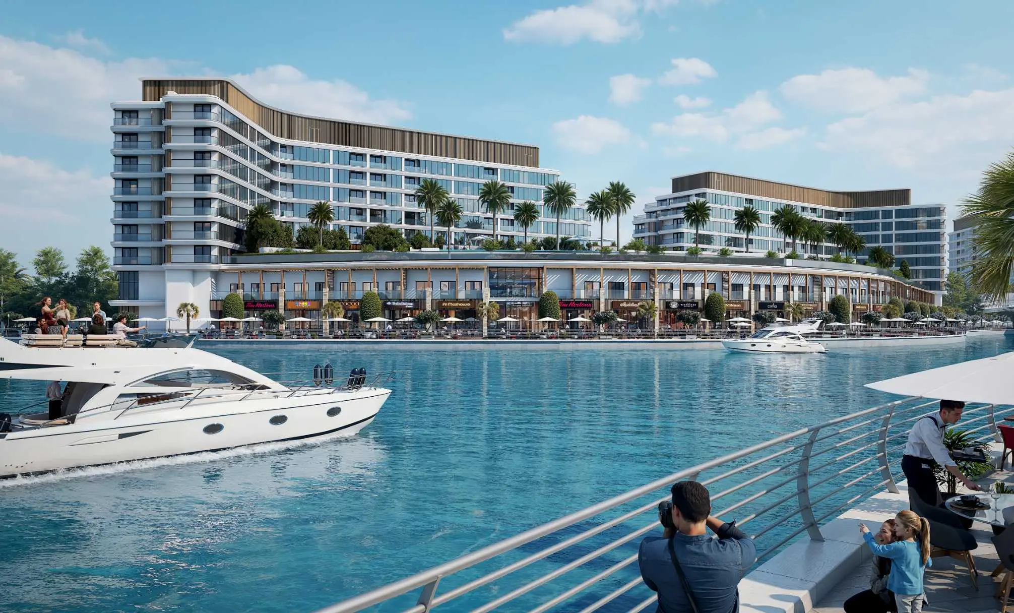 Render of the blocks seen from a railing across the canal, with stacked curved balconies at the corner, palms on the podium and a yacht passing