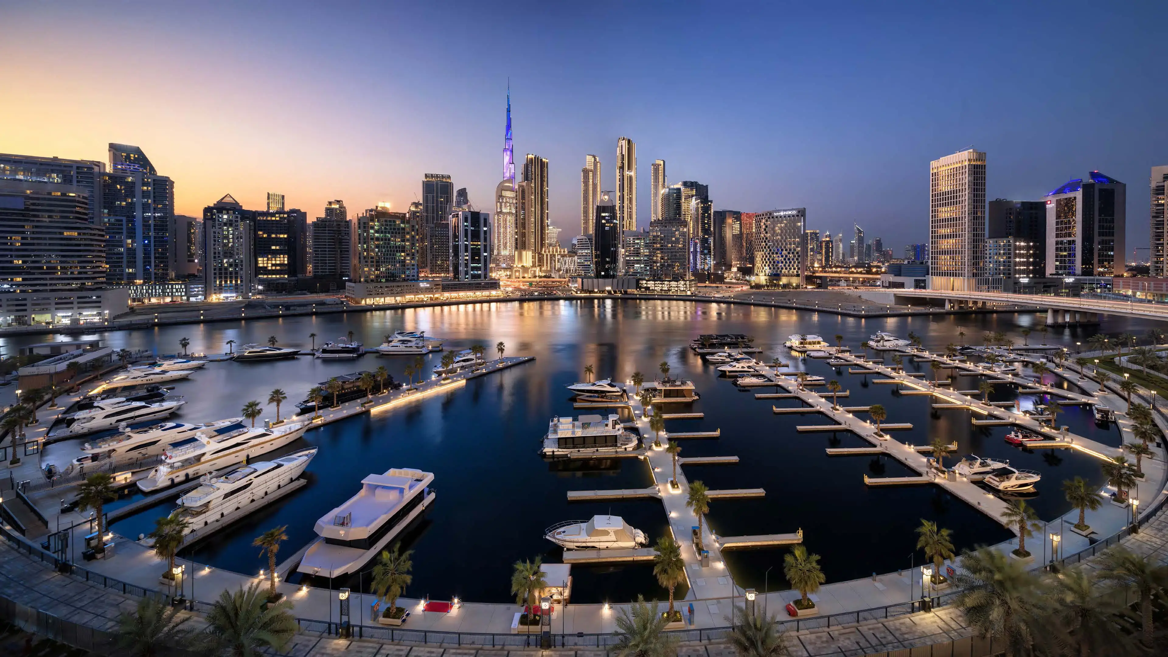 Render of the Marasi marina at dusk, yachts on lit pontoons, with the Burj Khalifa and Downtown towers behind